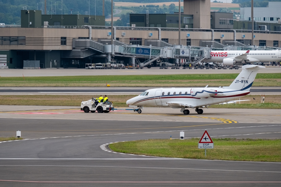 An aircraft tug tows a private jet along an airport taxiway